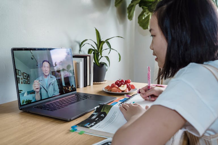 Young girl engaged in online learning via video call, studying with laptop and notes.
