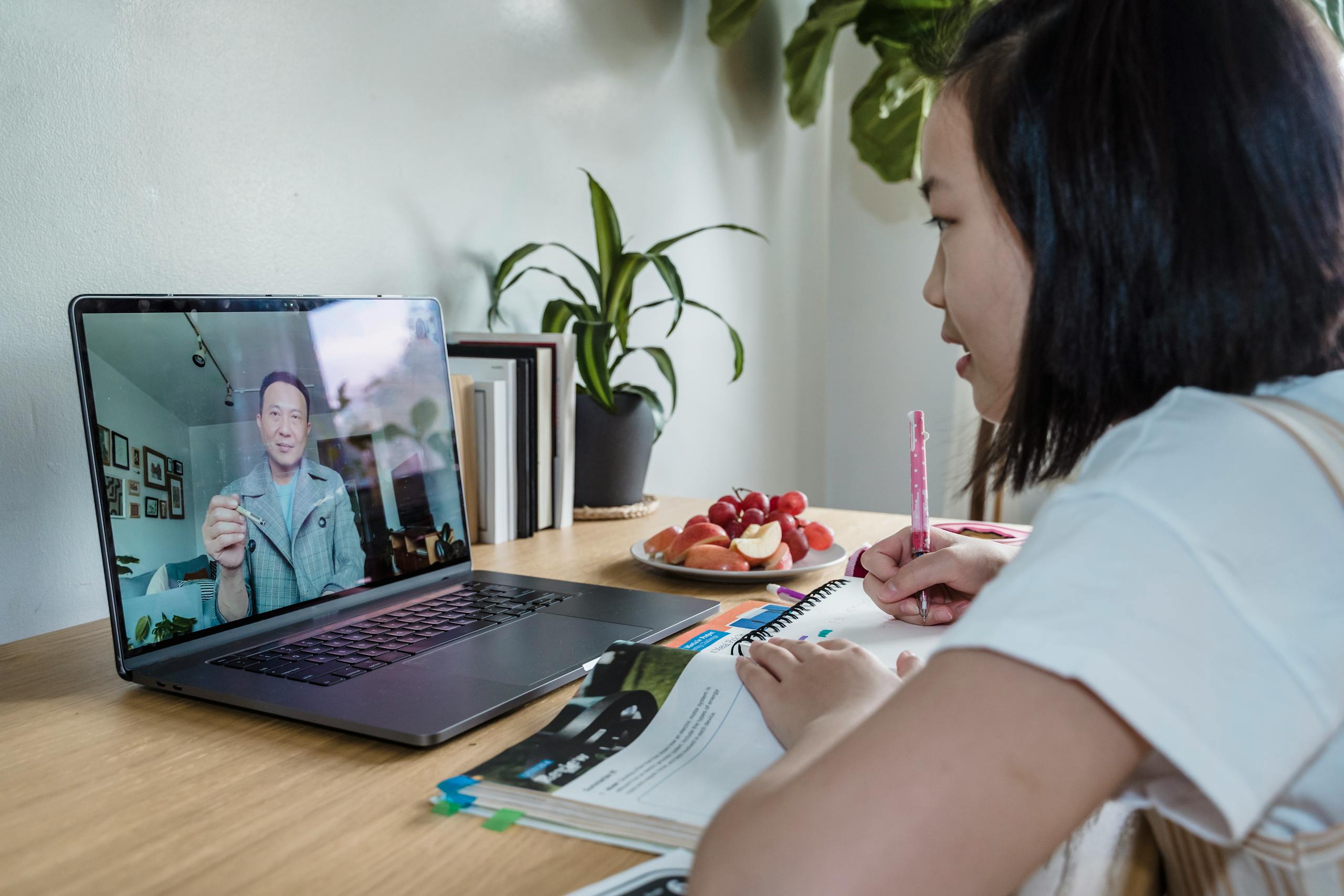 Young girl engaged in online learning via video call, studying with laptop and notes.