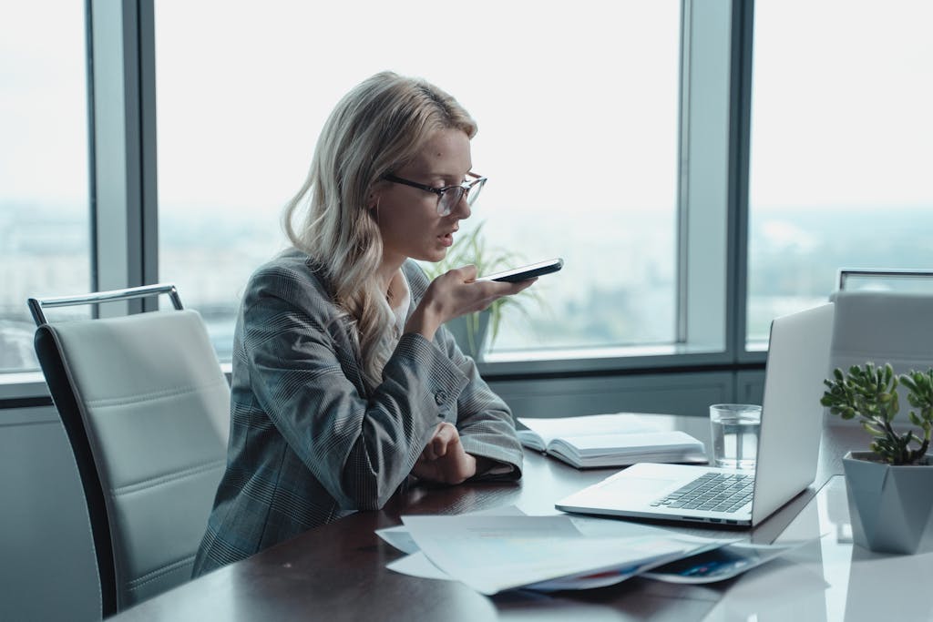 Young businesswoman with blonde hair using a smartphone for speech-to-text typing in a modern office setting.