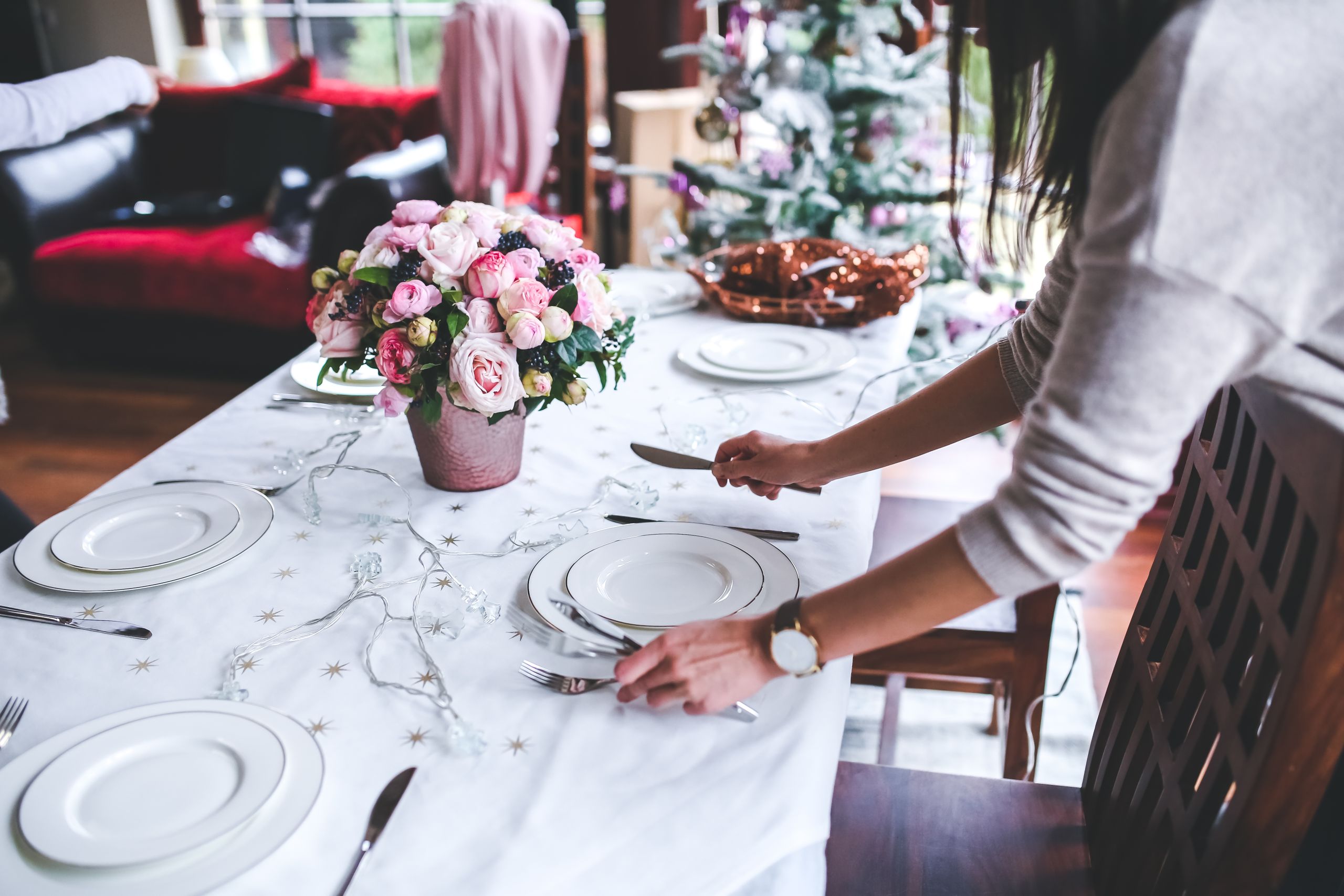 A woman sets a beautifully decorated dining table with flowers for a festive occasion indoors.