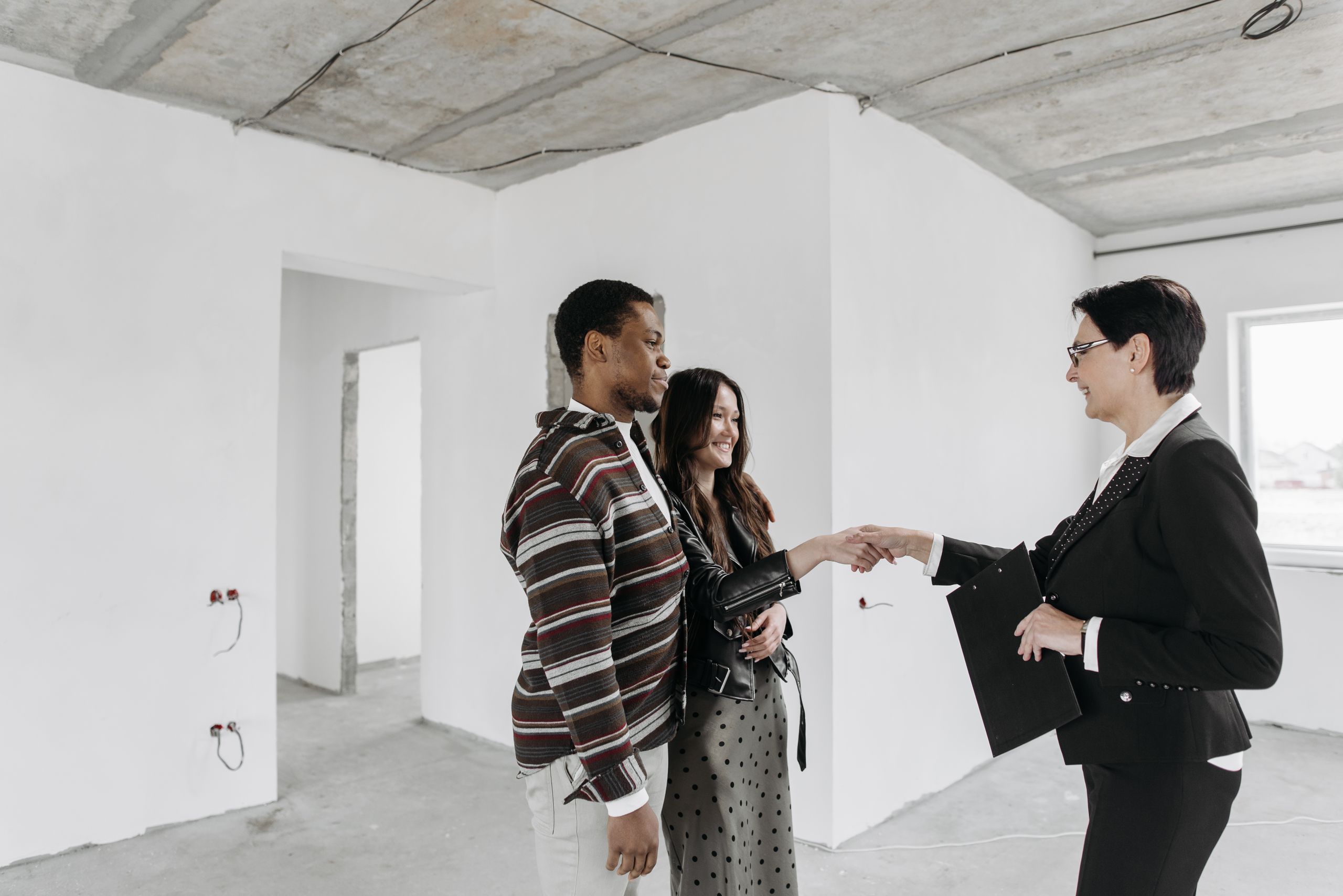 Happy couple shaking hands with real estate agent in unfinished home.