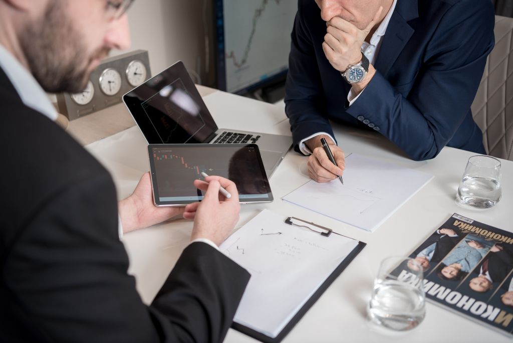 Two businessmen discussing financial charts on a tablet in a modern office setting.