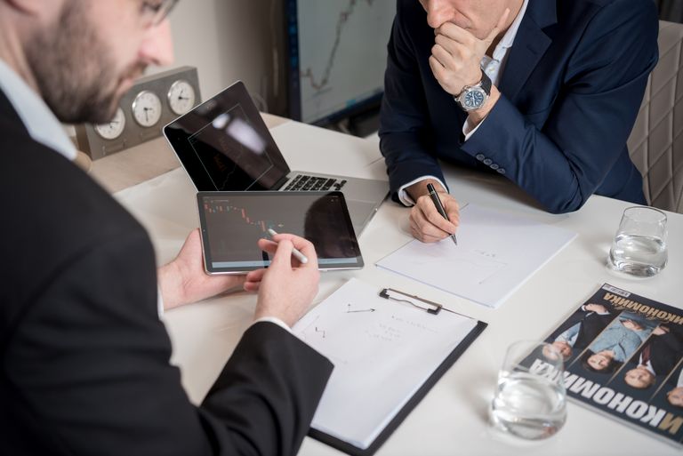 Two businessmen discussing financial charts on a tablet in a modern office setting.