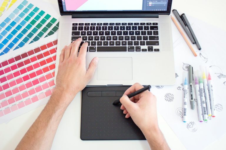 A person using a digital drawing tablet and laptop with color swatches and markers