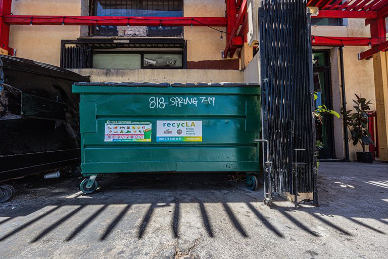 Front view of a green dumpster outside an urban building under daylight.