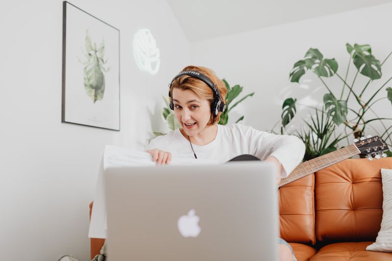 Young woman playing guitar and using laptop in a cozy living room.