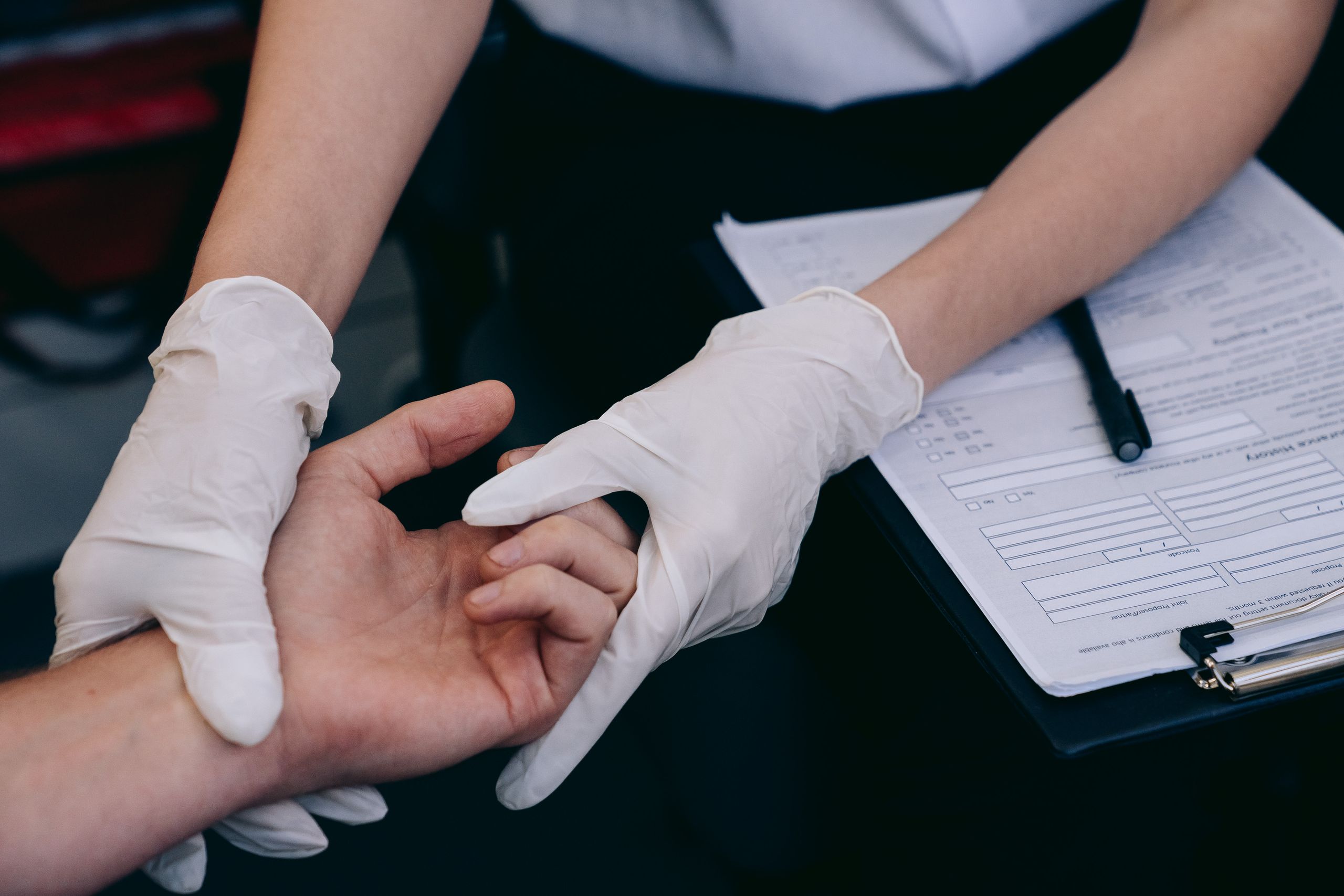 A healthcare worker wearing gloves examines a patient's hand during a medical procedure.