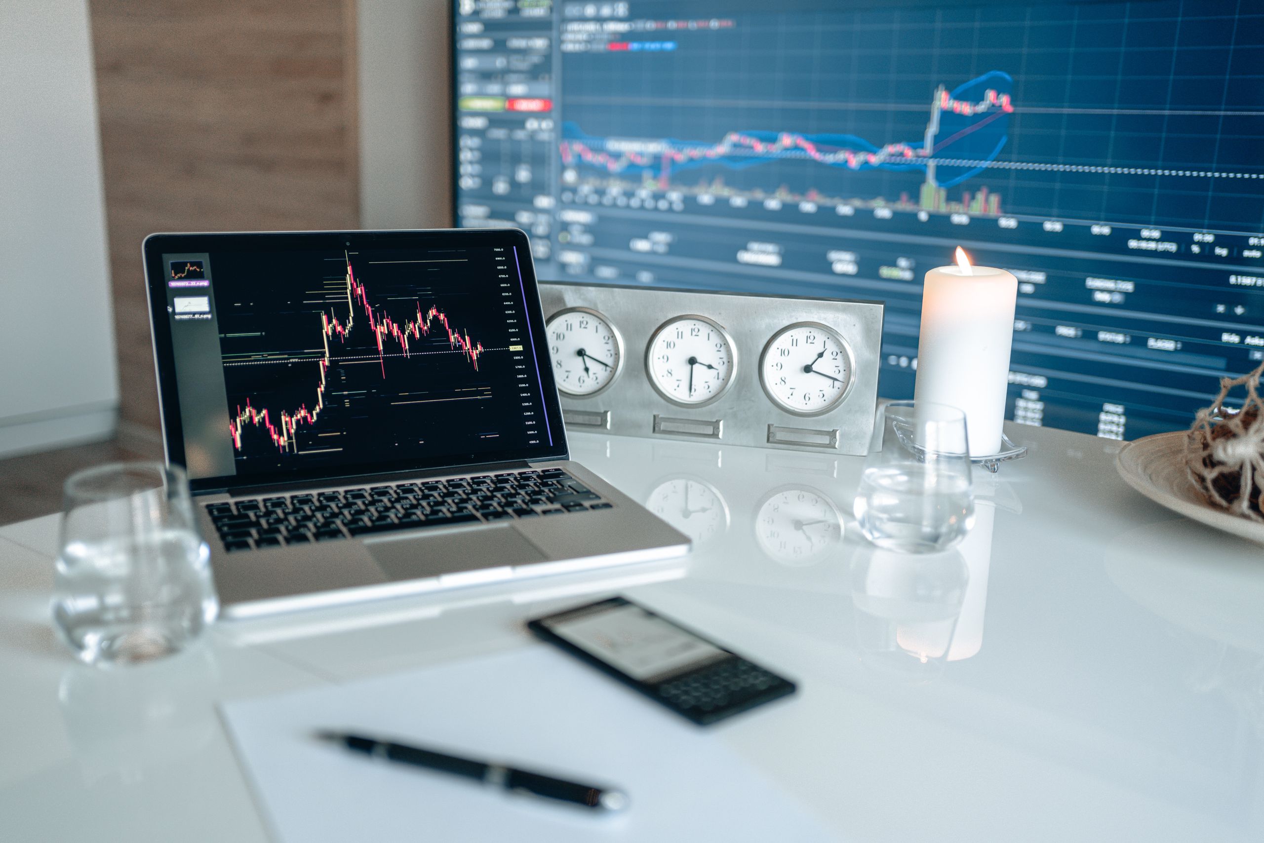 A modern workspace featuring financial charts and multiple clocks on a white table, ideal for trading.