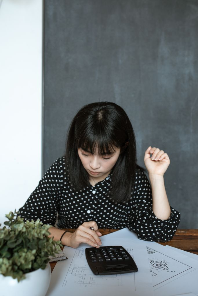 Asian woman calculating finance in modern office, focusing on documents and design work.