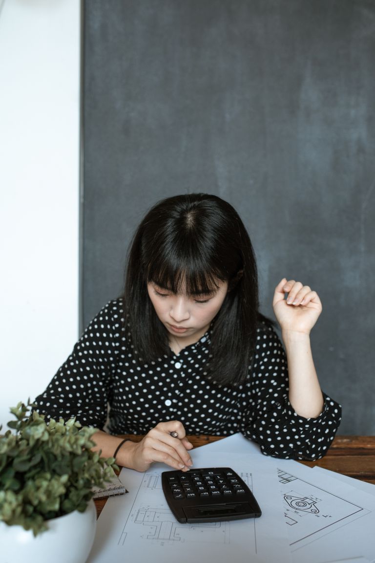 Asian woman calculating finance in modern office, focusing on documents and design work.