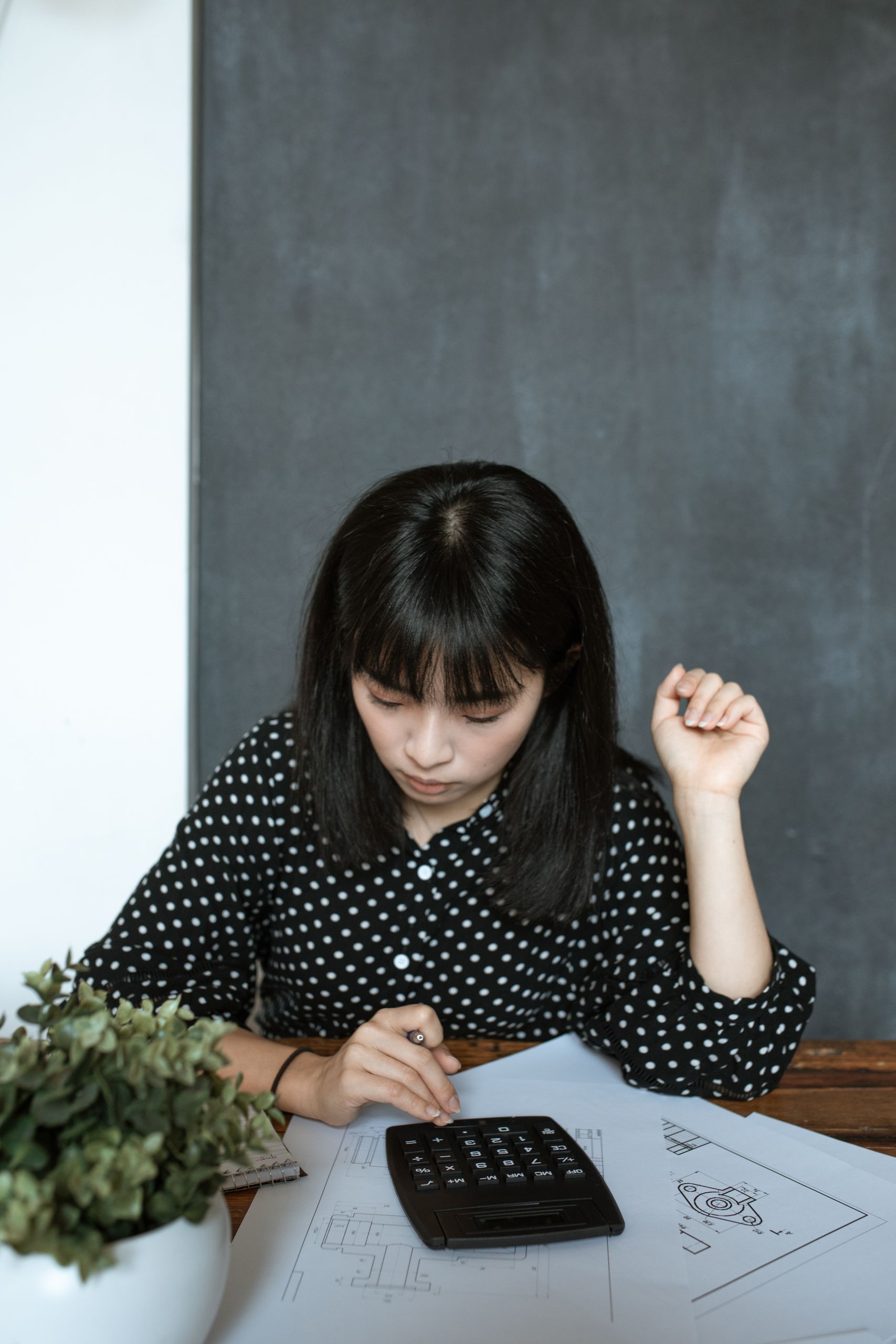 Asian woman calculating finance in modern office, focusing on documents and design work.