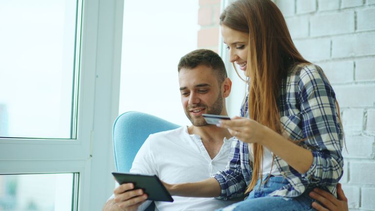 Couple shopping online using a tablet and credit card, enjoying time together indoors.