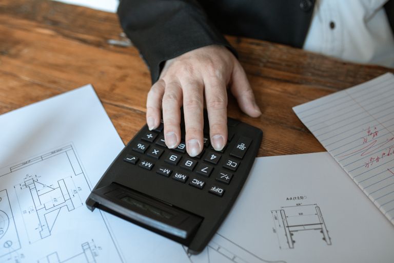 Hand using calculator for architectural calculations on blueprints.