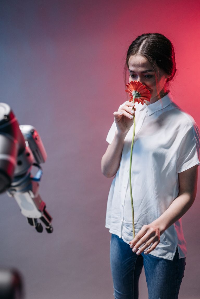 A woman interacts with a robot while holding a red flower, blending nature and technology.