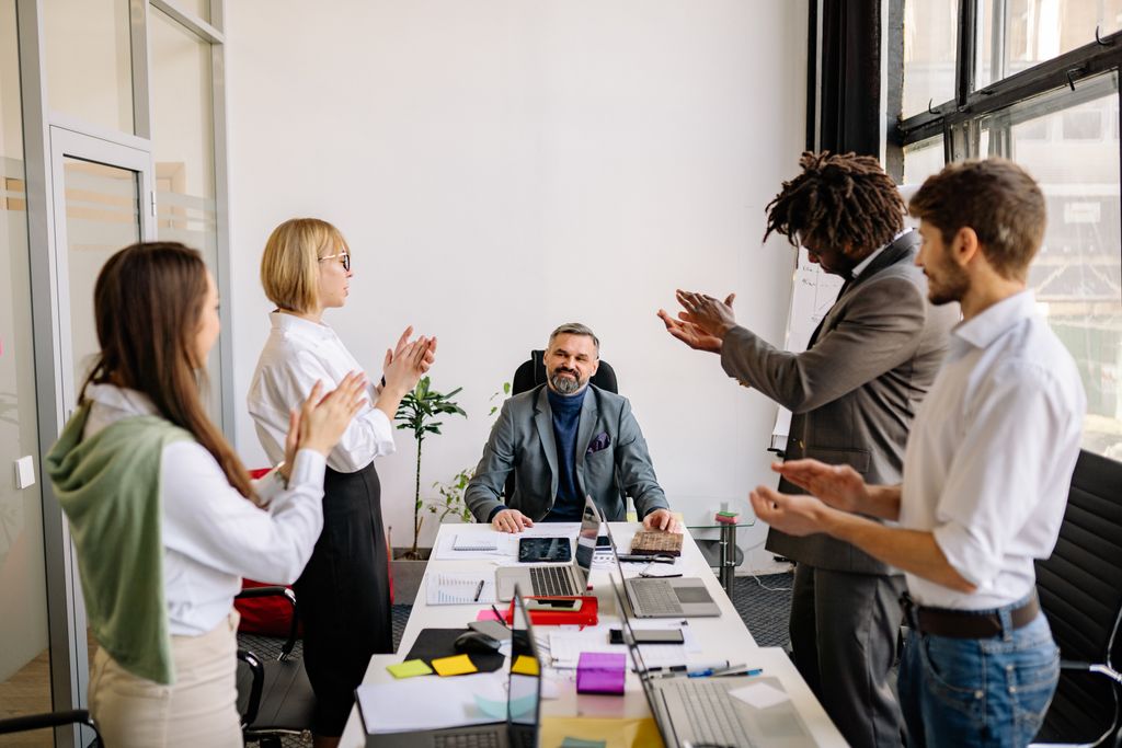Diverse business team applauding senior leader in modern office setting.