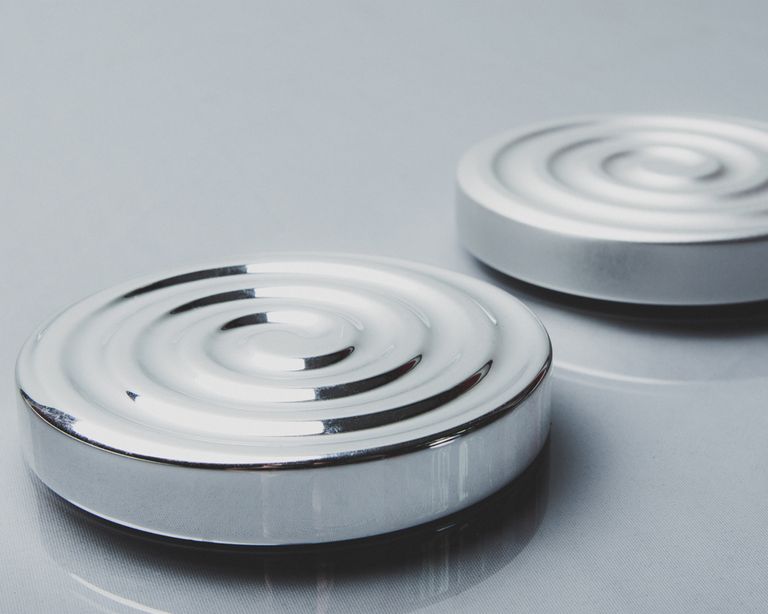 Two minimalist circular steel objects with concentric design on a reflective surface.