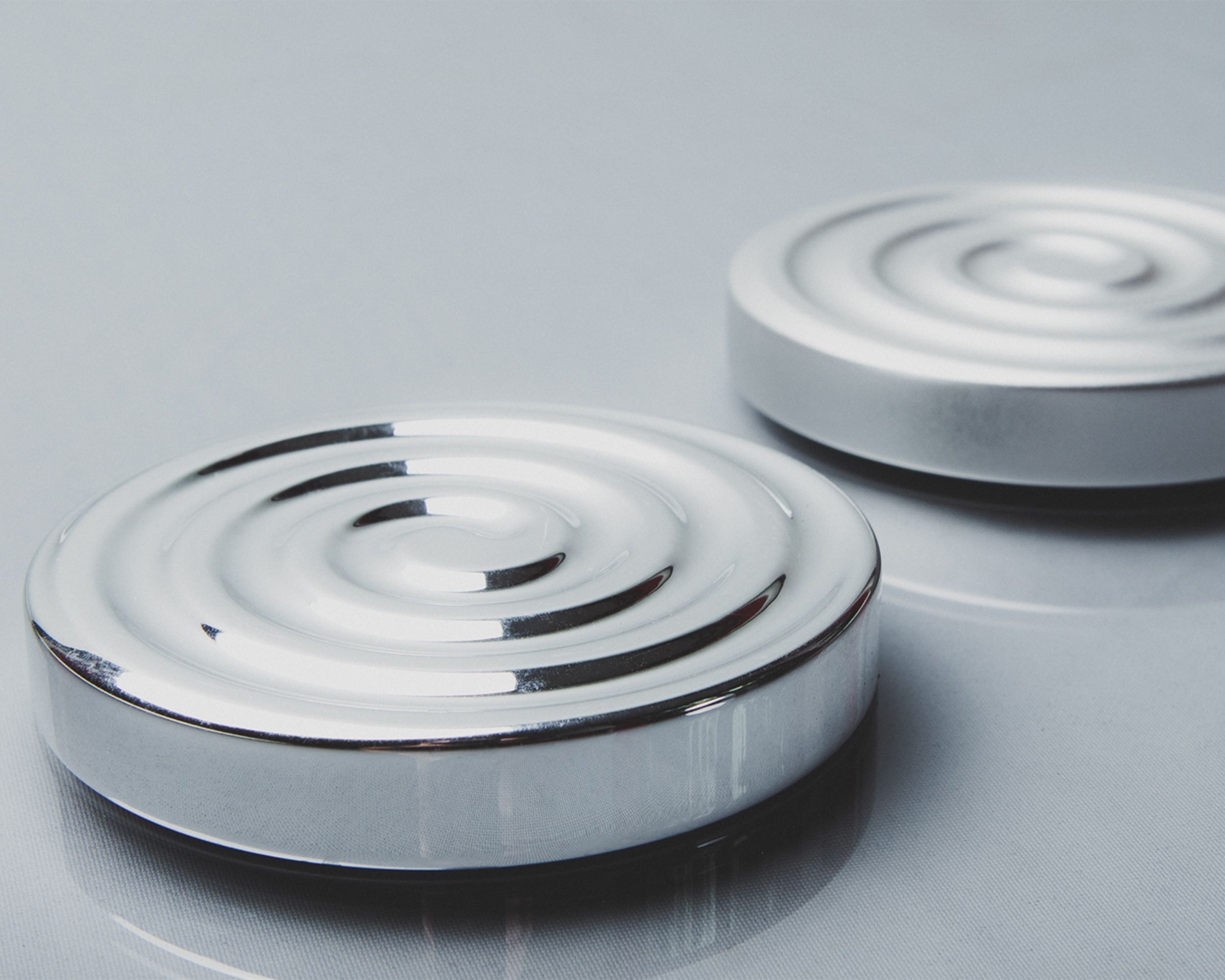Two minimalist circular steel objects with concentric design on a reflective surface.